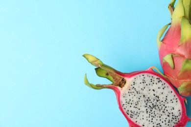 Photo of Delicious cut and whole dragon fruits (pitahaya) on light blue background, flat lay. Space for text