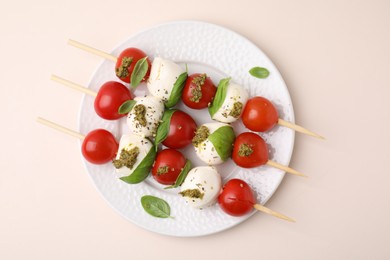 Photo of Caprese skewers with tomatoes, mozzarella balls, basil and pesto sauce on beige background, top view