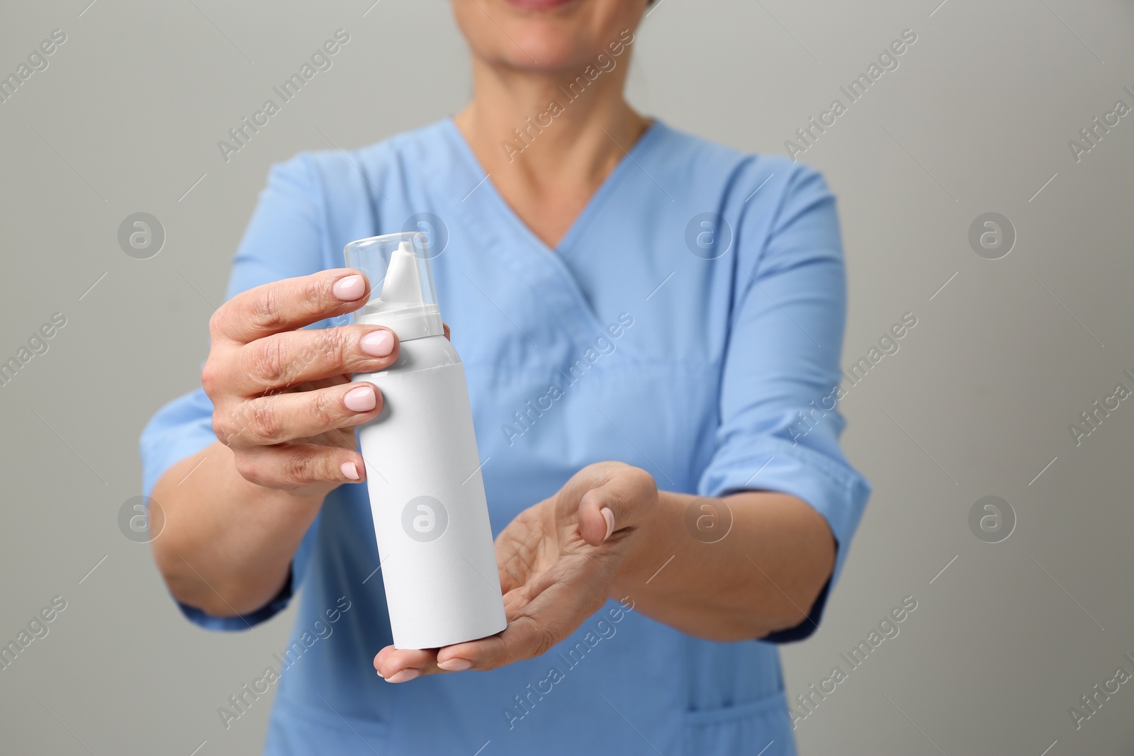 Photo of Woman holding nasal spray against light grey background, closeup