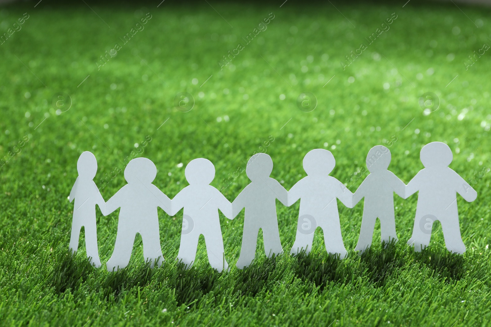 Photo of Paper people chain on green grass. Unity concept