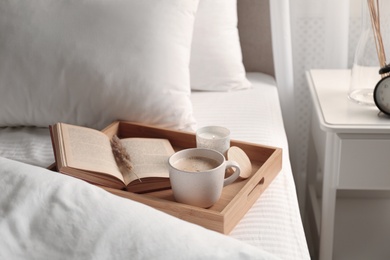 Photo of Cup of aromatic coffee, book and candle on bed with soft blanket indoors