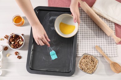 Photo of Making delicious baklava. Woman buttering baking pan at white wooden table, closeup