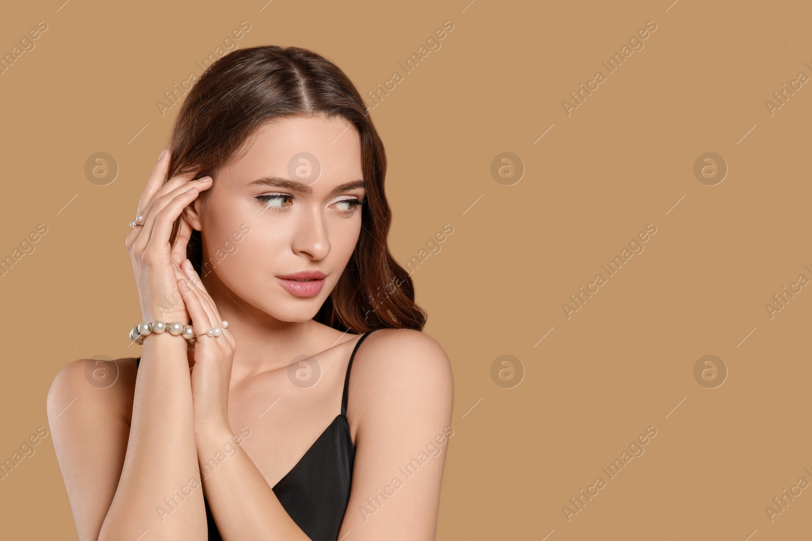 Photo of Young woman wearing elegant pearl jewelry on brown background, space for text