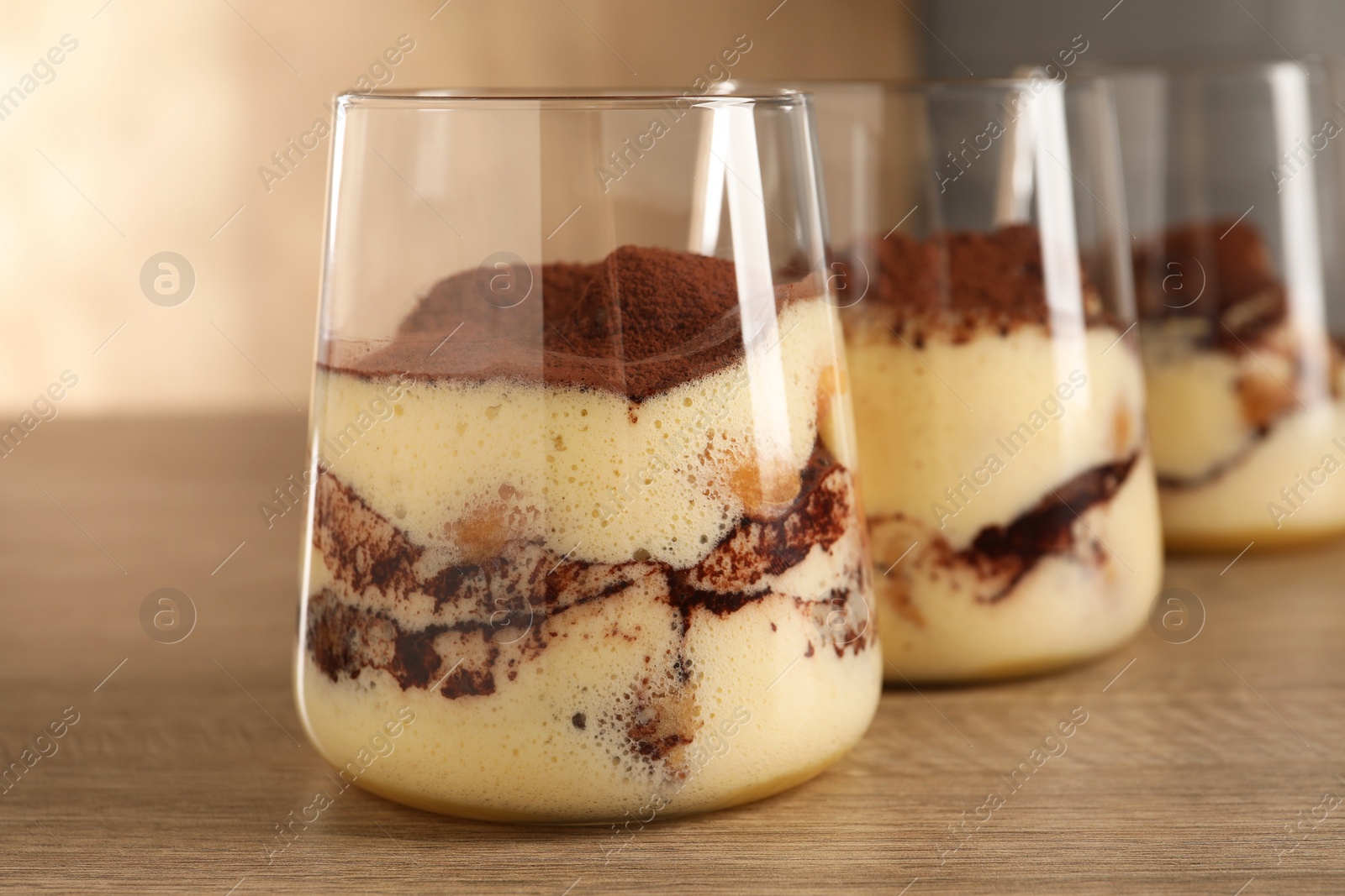 Photo of Delicious tiramisu in glasses on wooden table, closeup