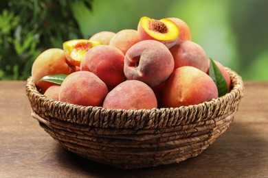 Cut and whole fresh ripe peaches in basket on wooden table against blurred background, closeup