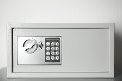 Photo of Closed steel safe on grey table against light background