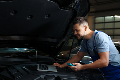 Photo of Mechanic with laptop doing car diagnostic at automobile repair shop