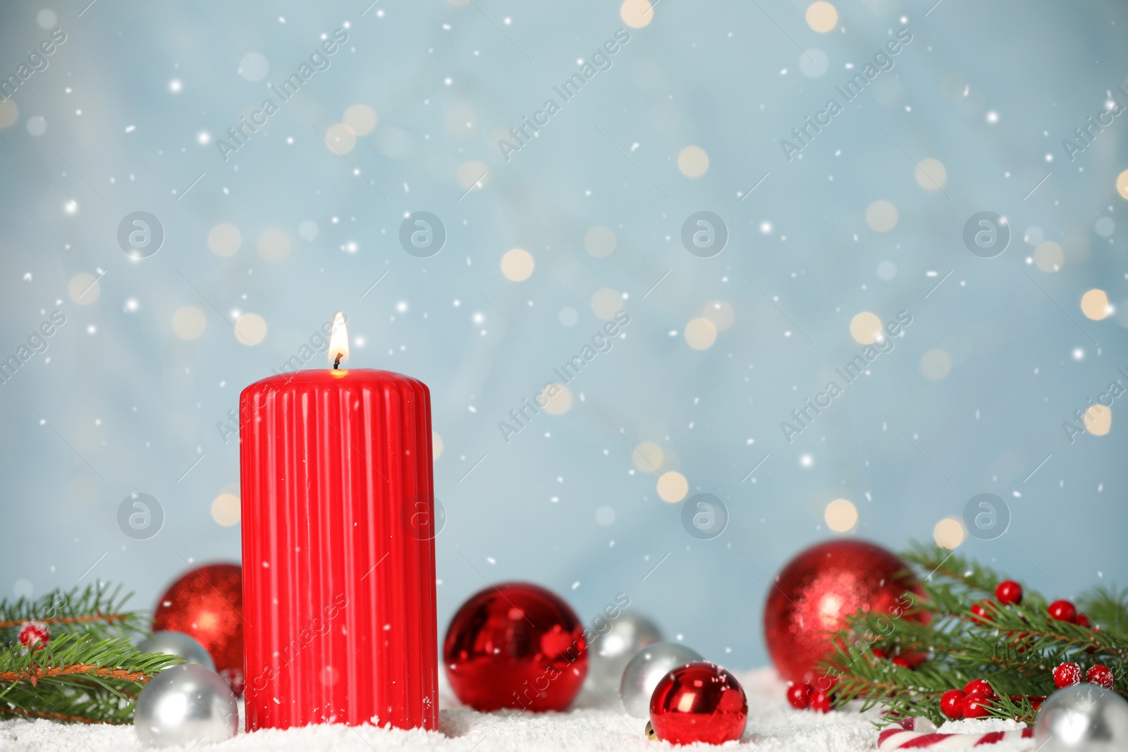 Photo of Snow falling on burning candle and festive decor against light blue background with blurred lights, space for text. Christmas eve