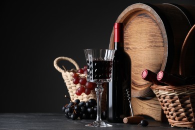 Photo of Glass of red wine, bottles, grapes and wooden barrel on black table. Space for text