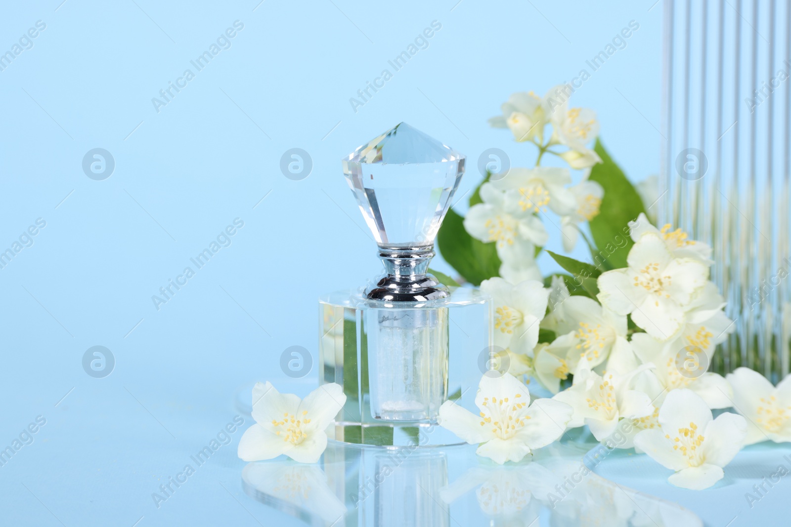 Photo of Aromatic perfume in bottle and beautiful jasmine flowers on light blue background, closeup. Space for text