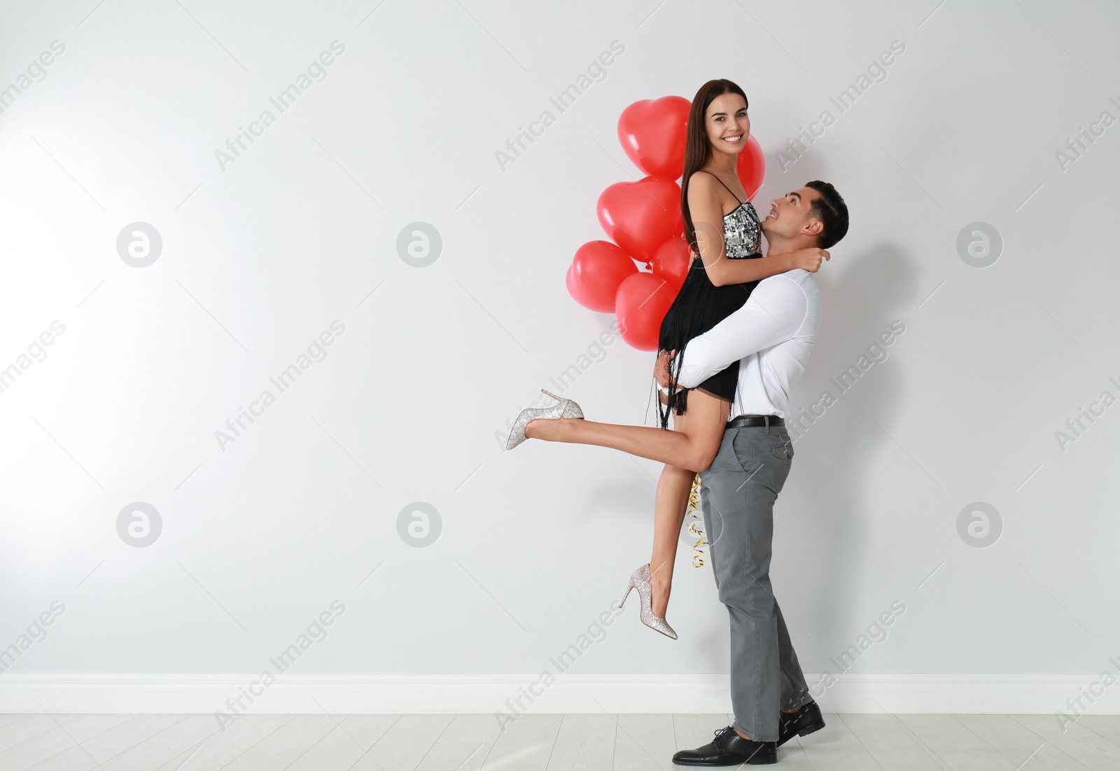 Photo of Beautiful couple with heart shaped balloons near light wall, space for text