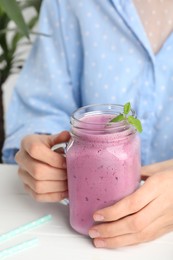 Photo of Woman with mason jar of delicious blackberry smoothie at white table indoors, closeup