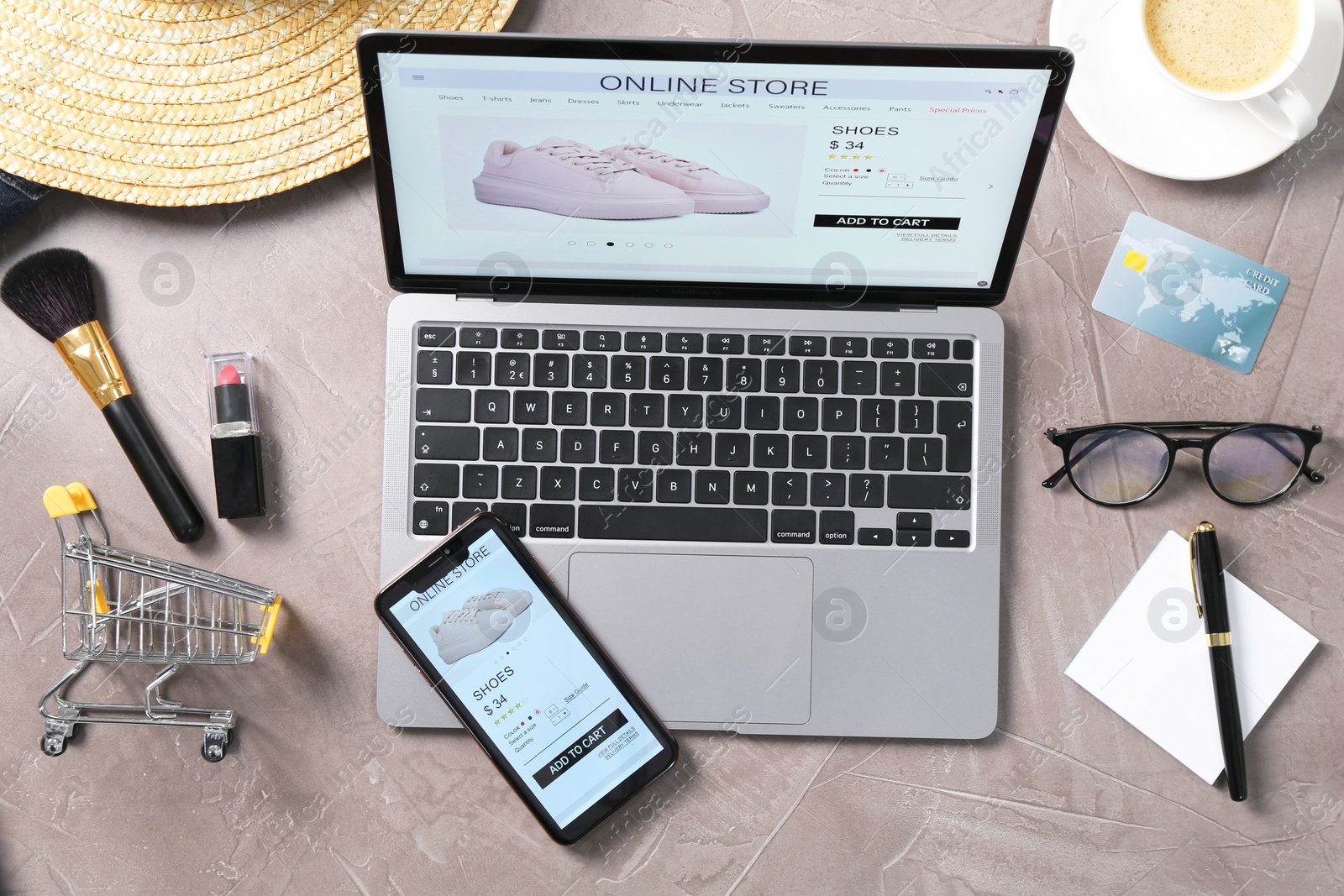 Photo of Online store website on laptop screen. Computer, smartphone, coffee and different items on grey table, flat lay