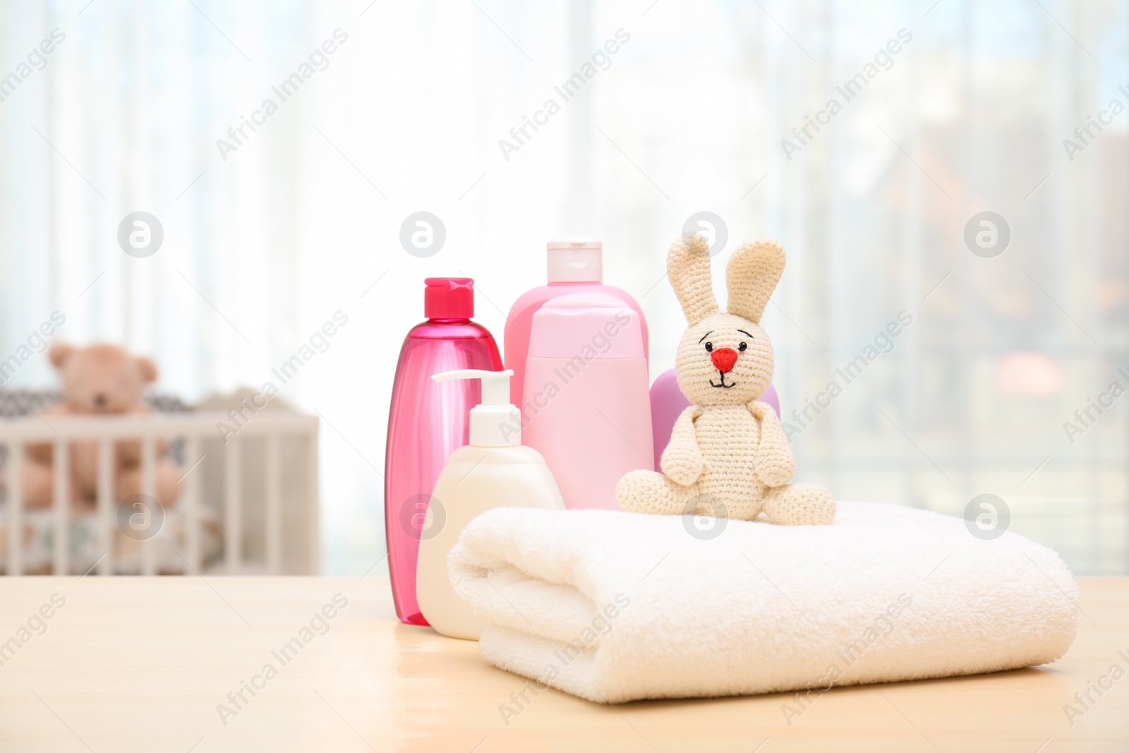 Photo of Baby cosmetic products, toy and towel on table indoors. Space for text