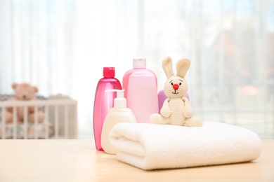 Photo of Baby cosmetic products, toy and towel on table indoors. Space for text