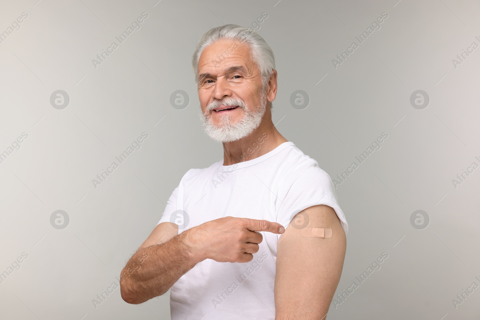 Photo of Senior man pointing at adhesive bandage after vaccination on light grey background