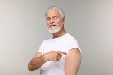 Senior man pointing at adhesive bandage after vaccination on light grey background