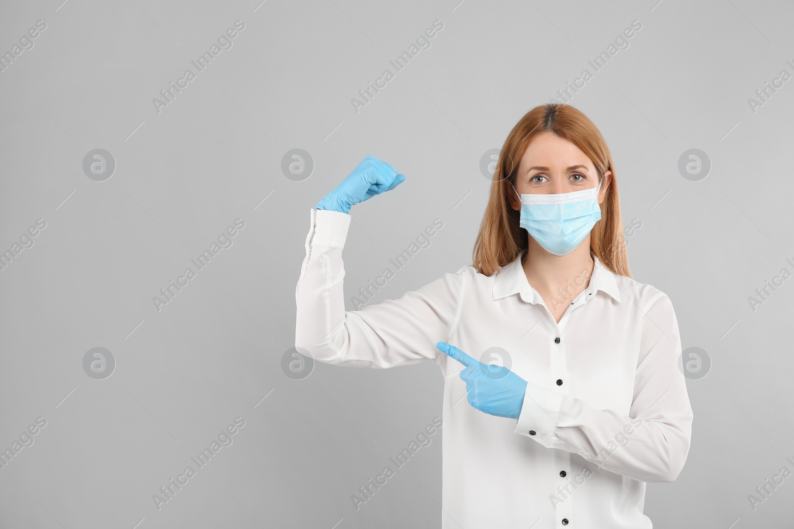Photo of Woman with protective mask and gloves showing muscles on light grey background, space for text. Strong immunity concept