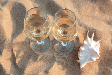 Photo of Glasses of tasty wine and seashell on sand, above view