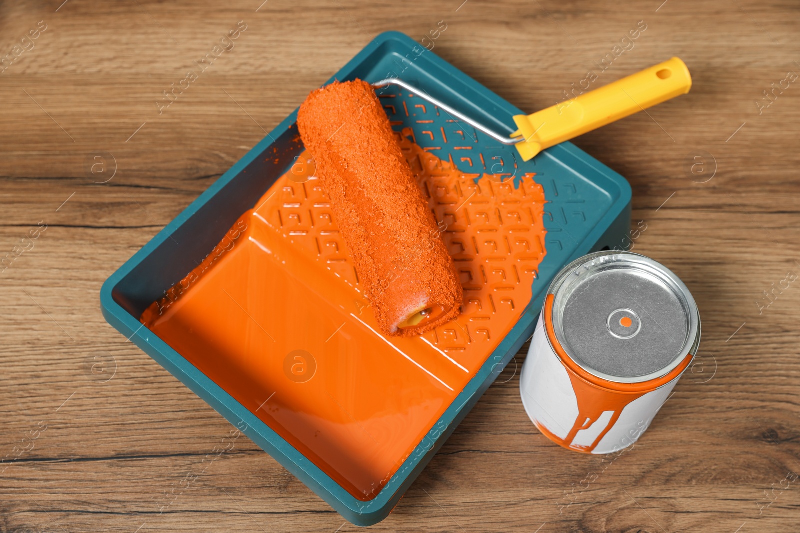 Photo of Can of orange paint, tray and roller on wooden table