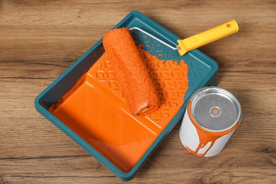 Can of orange paint, tray and roller on wooden table