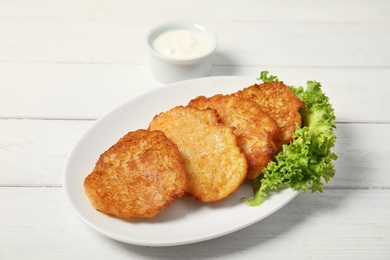 Plate with tasty potato fritters and sauce on wooden table