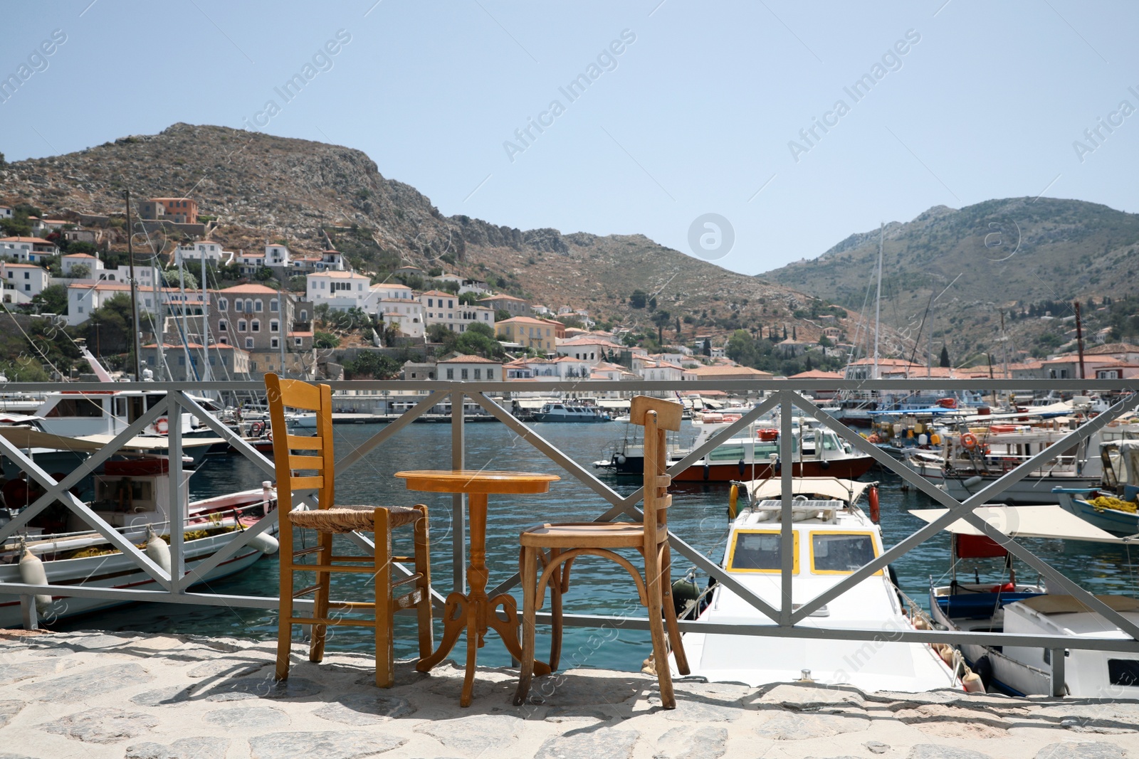 Photo of Wooden table and chairs near port with different boats on sunny day