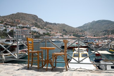 Wooden table and chairs near port with different boats on sunny day