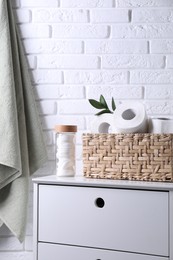 Photo of Toilet paper rolls in wicker basket, floral decor and cotton pads on chest of drawers