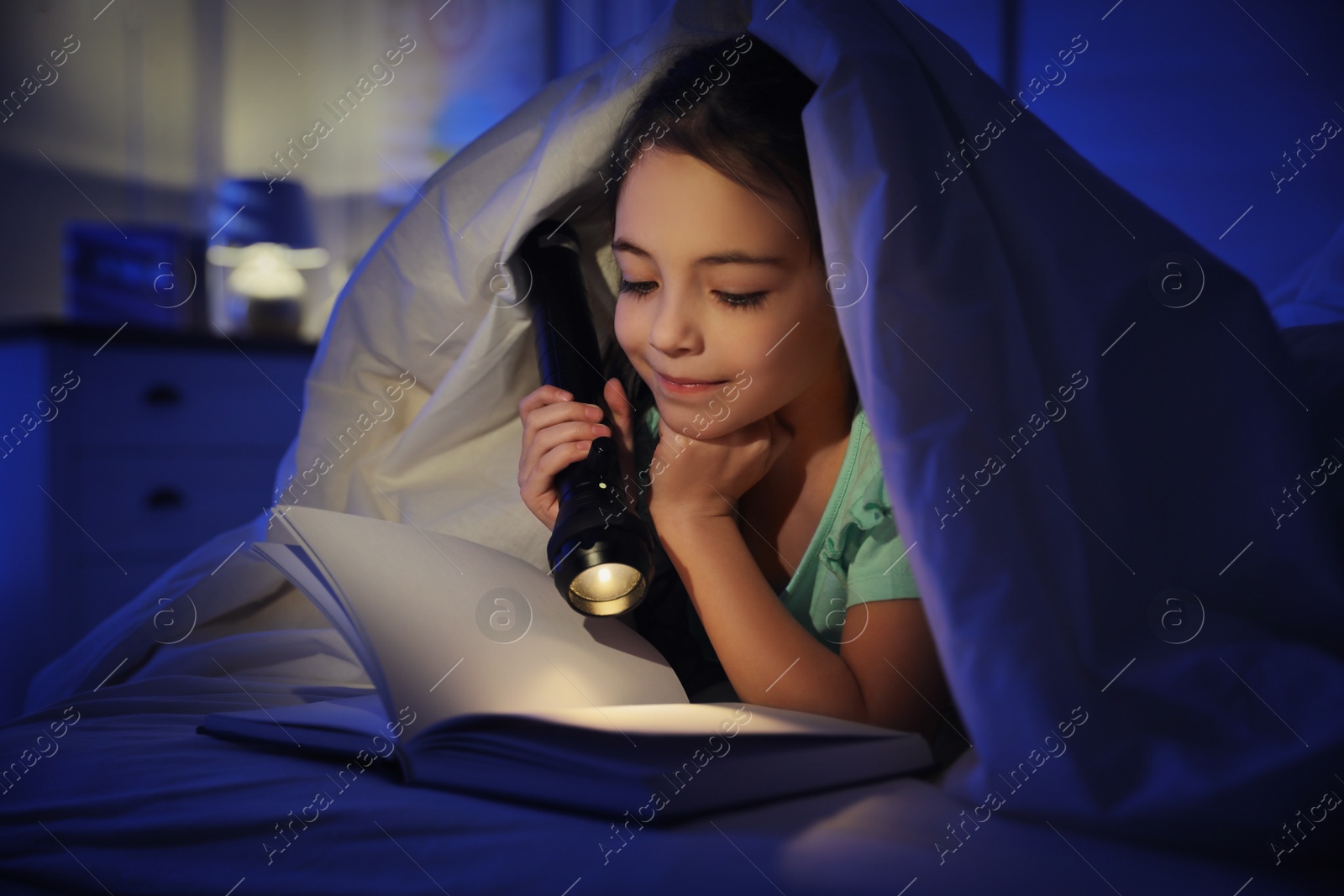 Photo of Little girl with flashlight reading fairy tale in dark bedroom