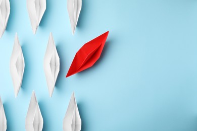 Red paper boat floating away from others on light blue background, flat lay with space for text. Uniqueness concept