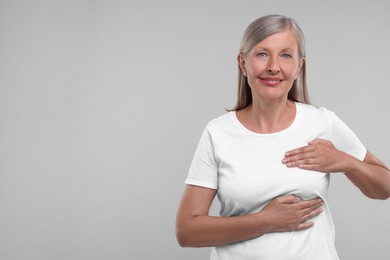 Photo of Beautiful senior woman doing breast self-examination on light grey background, space for text