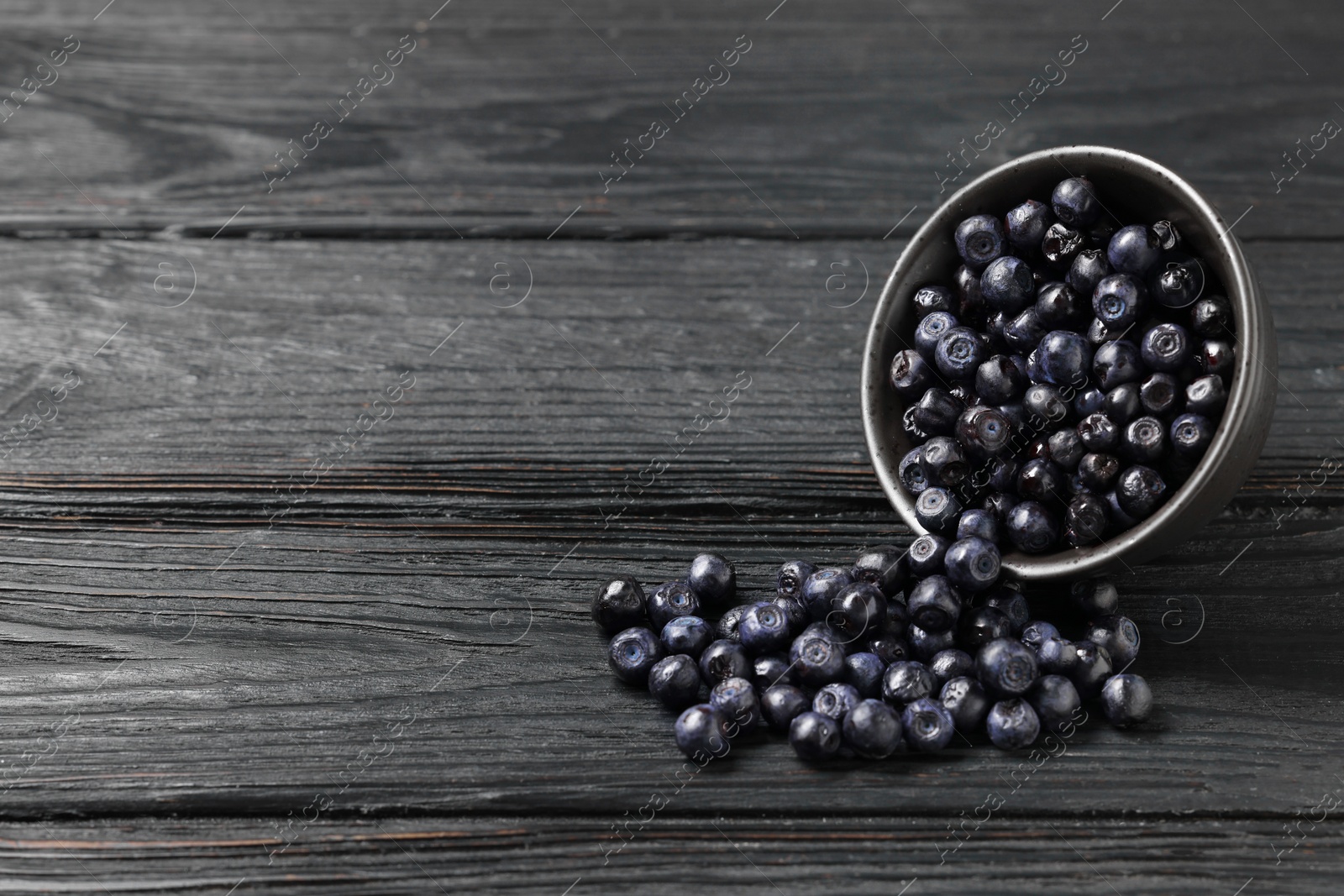 Photo of Ripe bilberries on dark wooden table. Space for text