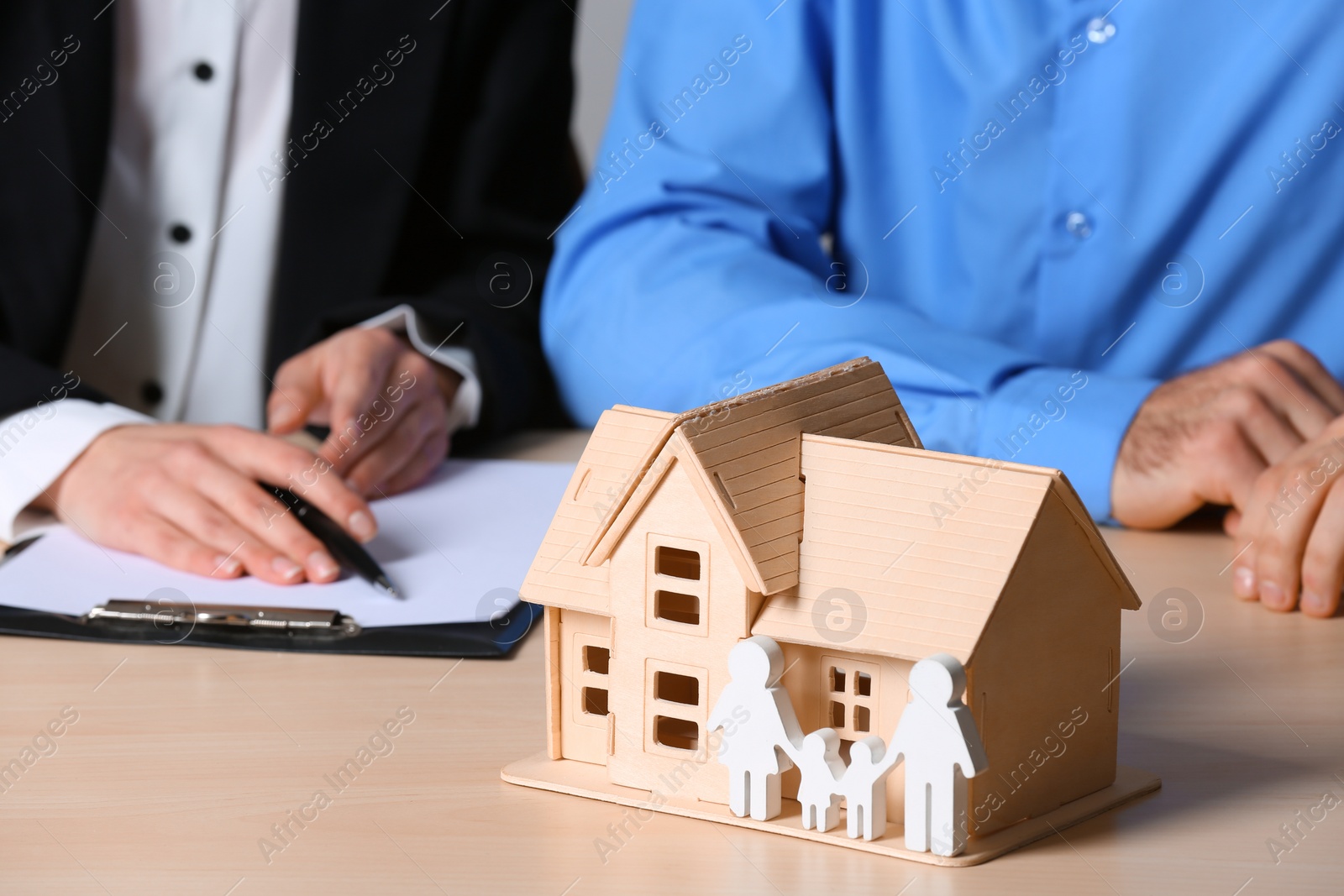 Photo of Real estate agent working with client at table, focus on house and family figures. Home insurance