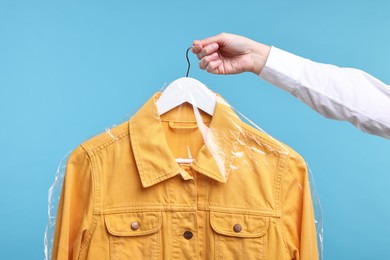 Dry-cleaning service. Woman holding shirt in plastic bag on light blue background, closeup