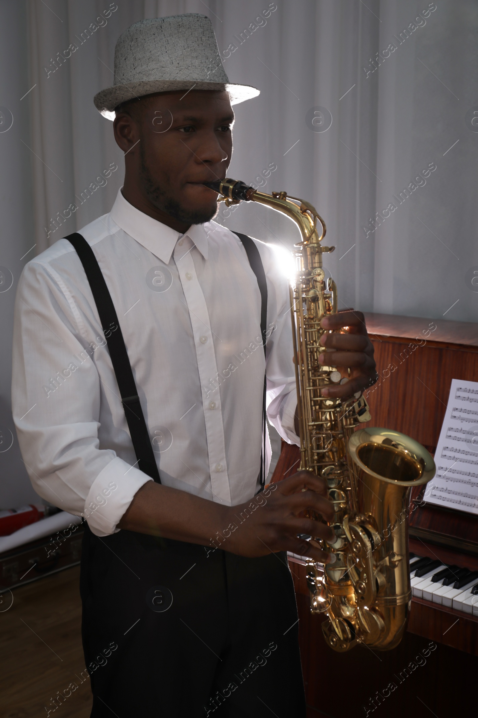 Photo of African-American man playing saxophone indoors. Talented musician