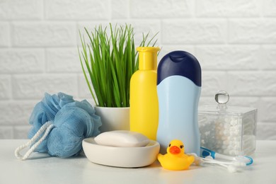 Different baby bath accessories and cosmetic products on white table against brick wall