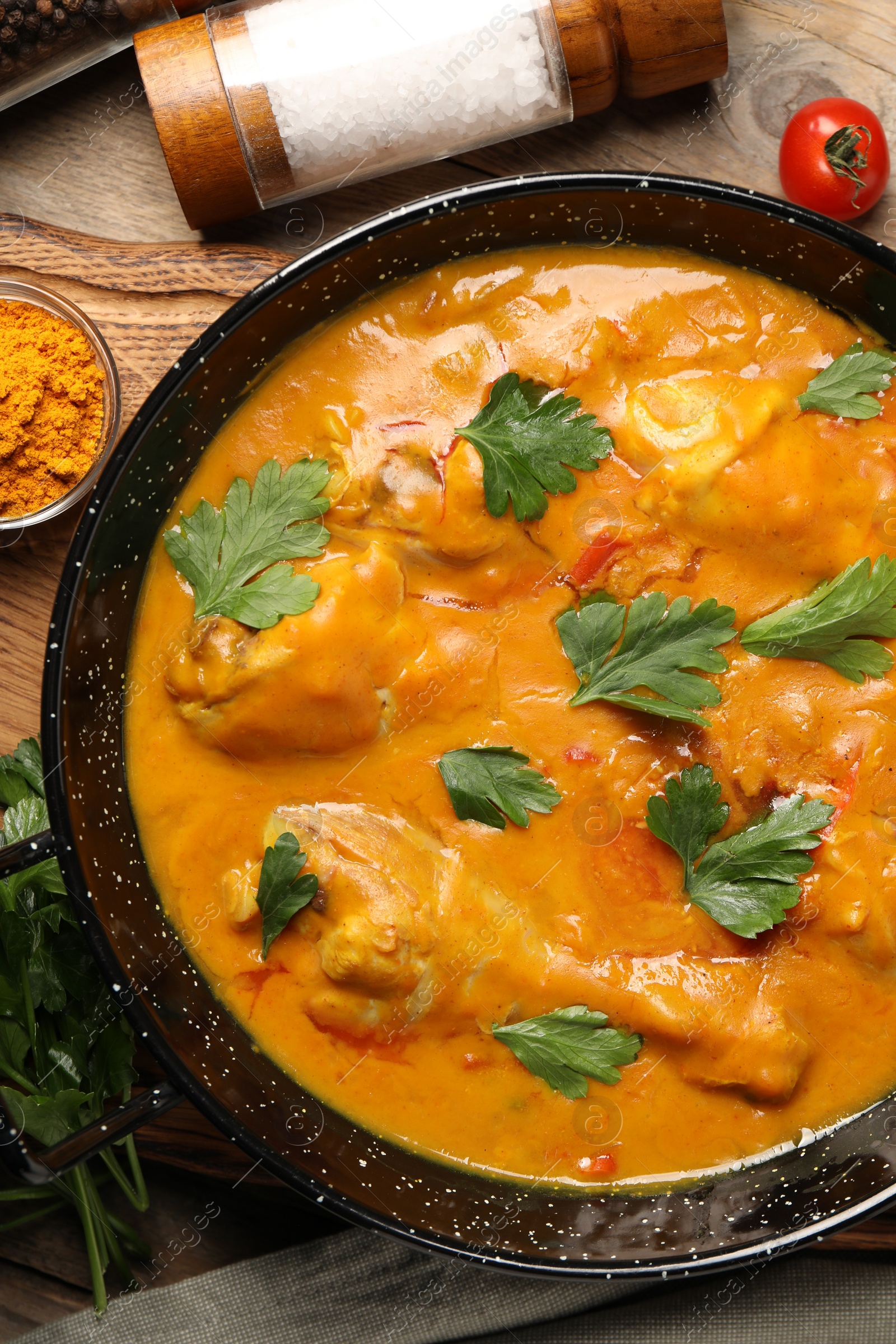 Photo of Tasty chicken curry with parsley and ingredients on wooden table, flat lay