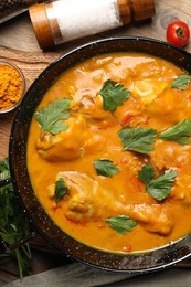 Tasty chicken curry with parsley and ingredients on wooden table, flat lay