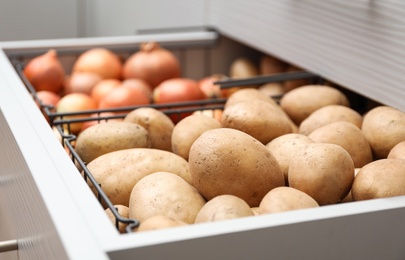 Photo of Open drawer with potatoes and onions, closeup. Orderly storage