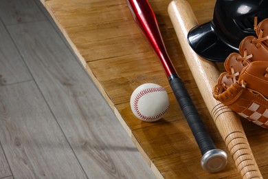 Photo of Baseball bats, batting helmet, leather glove and ball on wooden bench indoors, closeup. Space for text