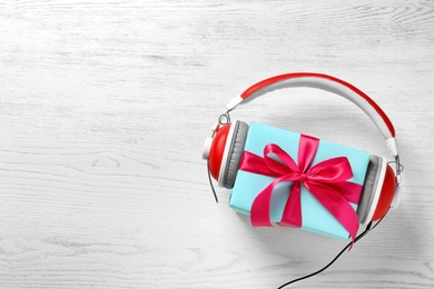 Flat lay composition with gift box and headphones on wooden background. Christmas music concept