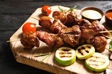 Photo of Delicious barbecued meat served with garnish and sauces on wooden board