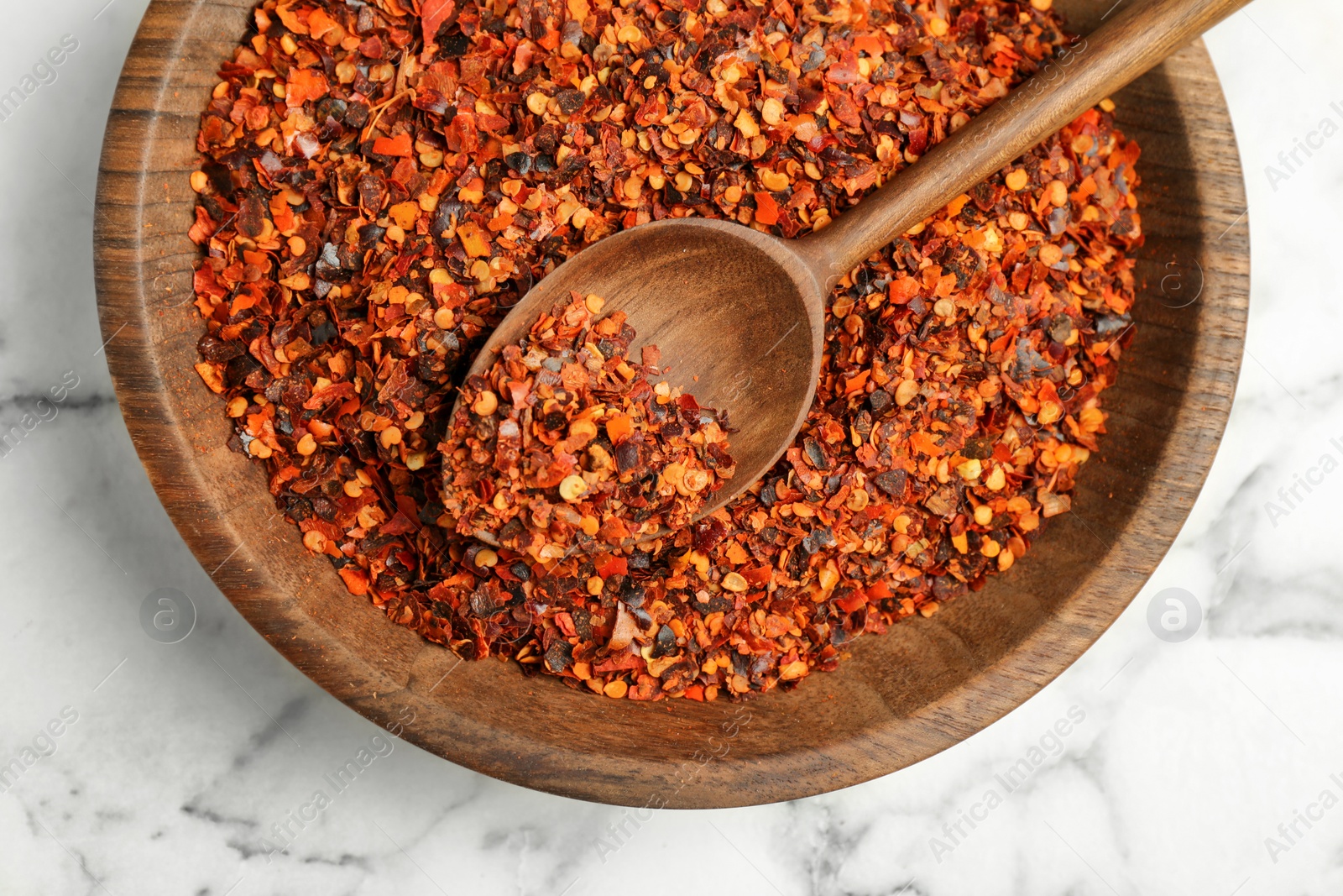 Photo of Plate with chili pepper flakes on marble background, top view