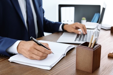 Photo of Lawyer working with laptop and notebook at table, closeup