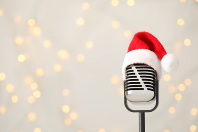Photo of Retro microphone with Santa hat against blurred lights, space for text. Christmas music