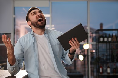 Emotional young man with tablet in office. Online hate concept