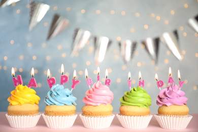 Photo of Birthday cupcakes with burning candles on pink table