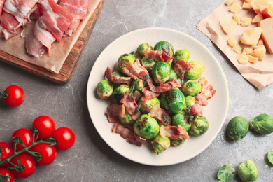 Photo of Delicious Brussels sprouts with bacon on marble table, flat lay