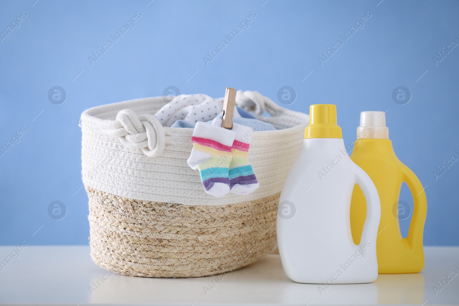 Photo of Detergents and children's clothes on white table near blue wall